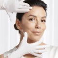 Dermatologista a segurar o rosto de uma mulher em fundo branco